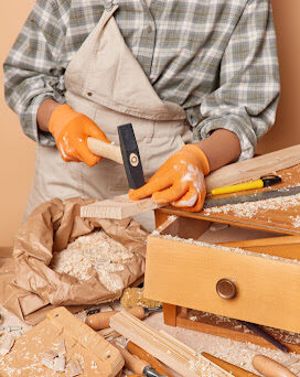 Cropped shot of unrecognizable skilled female jointer uses carpentry tools holds hammer involved in woodwork works in workshop dressed in checkered shirt overalls and gloves enjoys her profession SSUCv3H4sIAAAAAAAACpyRwW7DIAyG75P2DhHnRkpCk7R7lWoHB2iDSqEC0mmq+u4zkFQ+75b/s/3zO35+flQVmyBowb6qZ1KotTFLiB6idhZxs1u5V1YqT8nD86GhADRVSurovAZD4QRRzBZuCqFdjEn4lYssRIhLUCFlWZGAqC7oUeDbogQ+FV1thVzECSwxtiMsLFNmGyrm/5osH9/vhS/Kit8cmCzilVFQFjmVVnb9icrf6GqwSO3IVg8nwKQGTpzuXgttL2TMxTkfYRsTbrHRpwjv5Mw4d4fJpF98Rk+18RlCwHa5cfKQwJO7G3nHupgXWF2ZxEsk2XLeNUN7PPC+GUcU7dpQrjdr9MlxNiPU4qolXV2nBIzLg5j2XV+PwzDV+7EXNez7pj4r3g1ylJ0AiT/+9QcAAP//AwB02v0zpgIAAA==