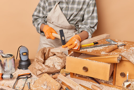 Cropped shot of unrecognizable skilled female jointer uses carpentry tools holds hammer involved in woodwork works in workshop dressed in checkered shirt overalls and gloves enjoys her profession SSUCv3H4sIAAAAAAAACpyRwW7DIAyG75P2DhHnRkpCk7R7lWoHB2iDSqEC0mmq+u4zkFQ+75b/s/3zO35+flQVmyBowb6qZ1KotTFLiB6idhZxs1u5V1YqT8nD86GhADRVSurovAZD4QRRzBZuCqFdjEn4lYssRIhLUCFlWZGAqC7oUeDbogQ+FV1thVzECSwxtiMsLFNmGyrm/5osH9/vhS/Kit8cmCzilVFQFjmVVnb9icrf6GqwSO3IVg8nwKQGTpzuXgttL2TMxTkfYRsTbrHRpwjv5Mw4d4fJpF98Rk+18RlCwHa5cfKQwJO7G3nHupgXWF2ZxEsk2XLeNUN7PPC+GUcU7dpQrjdr9MlxNiPU4qolXV2nBIzLg5j2XV+PwzDV+7EXNez7pj4r3g1ylJ0AiT/+9QcAAP//AwB02v0zpgIAAA==